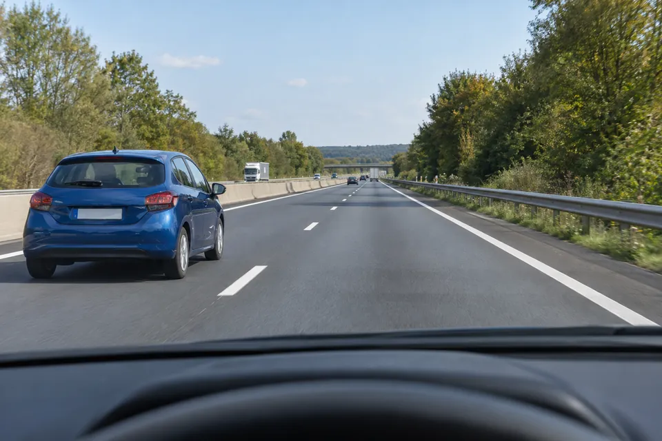 Une voiture bleue dépasse par la bande de gauche sur une autoroute.