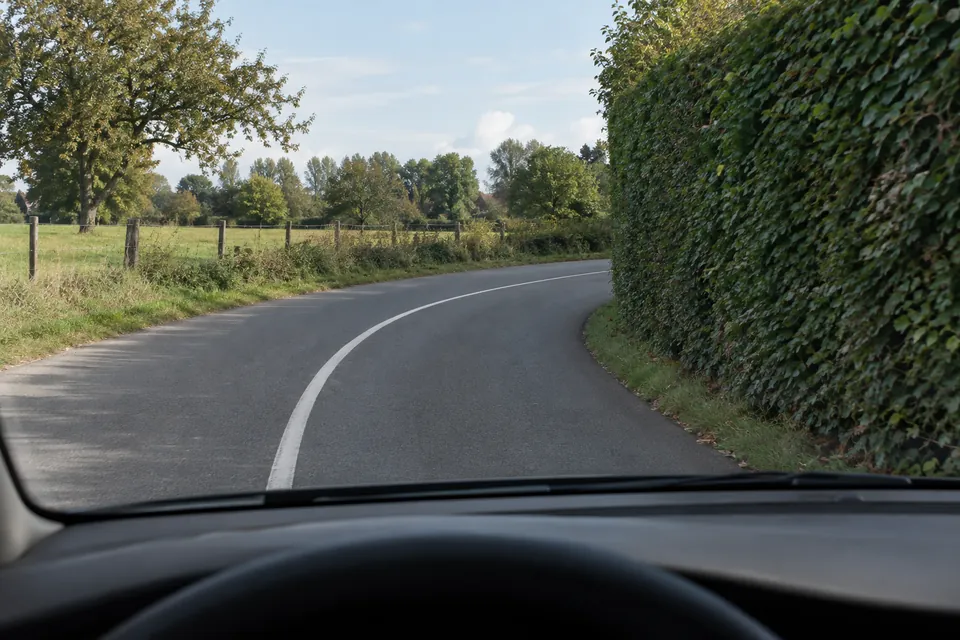 Virage à droite dont la suite est masquée par une haute haie le long de la chaussée.
