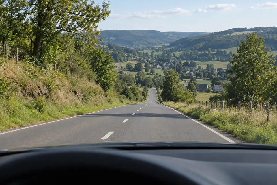 Route rurale descendant vers une vallée, vue depuis un véhicule dans la bande de droite.