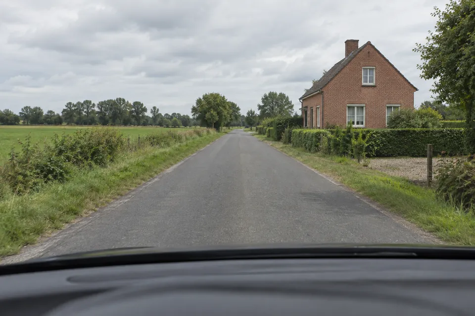 Maison isolée au bord d’une route de campagne, entourée de champs et sans panneau visible.