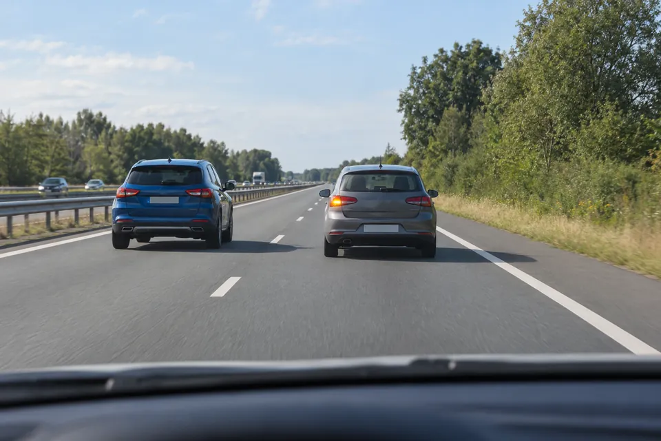 Voiture grise sur la bande droite avec son clignotant gauche allumé et voiture bleue sur la bande gauche.