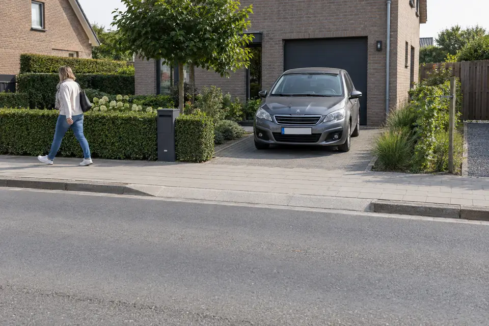 Voiture dans une allée privée devant un garage, avec un trottoir entre l’allée et la chaussée.