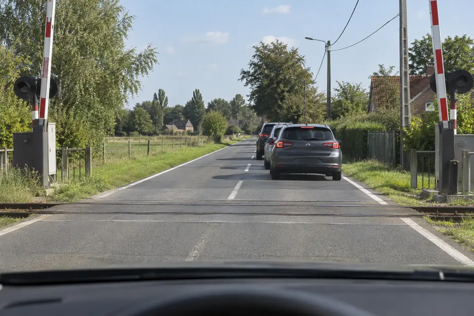 Passage à niveau aux barrières relevées, avec une file de voitures de l’autre côté des rails.