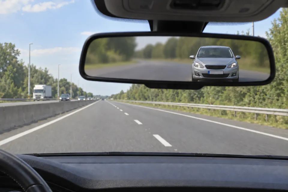 Une voiture apparaît dans le rétroviseur intérieur sur une autoroute.