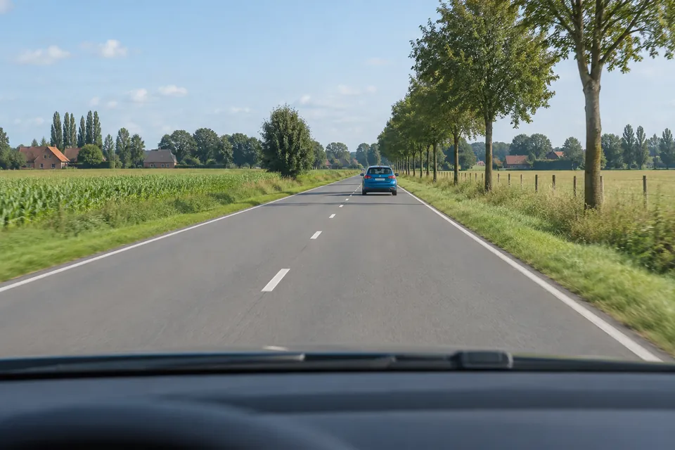 Voiture bleue devant le véhicule observateur sur une route dégagée par temps sec.