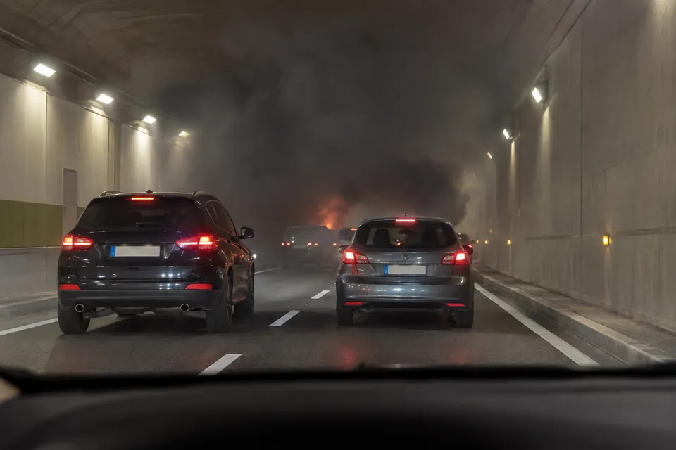 Voitures aux feux de freinage allumés dans un tunnel, avec une fumée sombre et un foyer lumineux plus loin.
