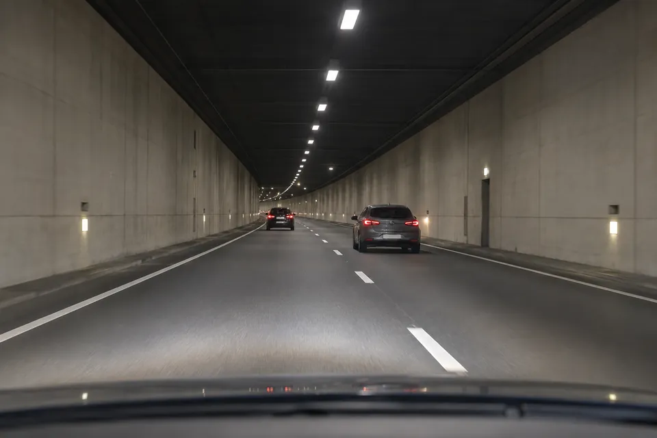 Deux voitures circulant dans un tunnel éclairé, vues depuis un véhicule derrière elles.