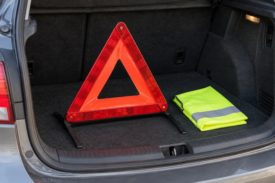 Triangle de présignalisation déplié et gilet réfléchissant posés dans un coffre ouvert.