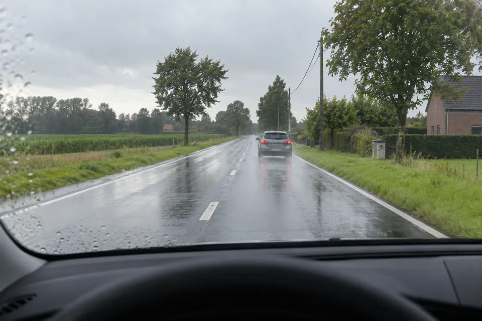 Voiture sur une chaussée mouillée, vue depuis le véhicule qui la suit sous la pluie.
